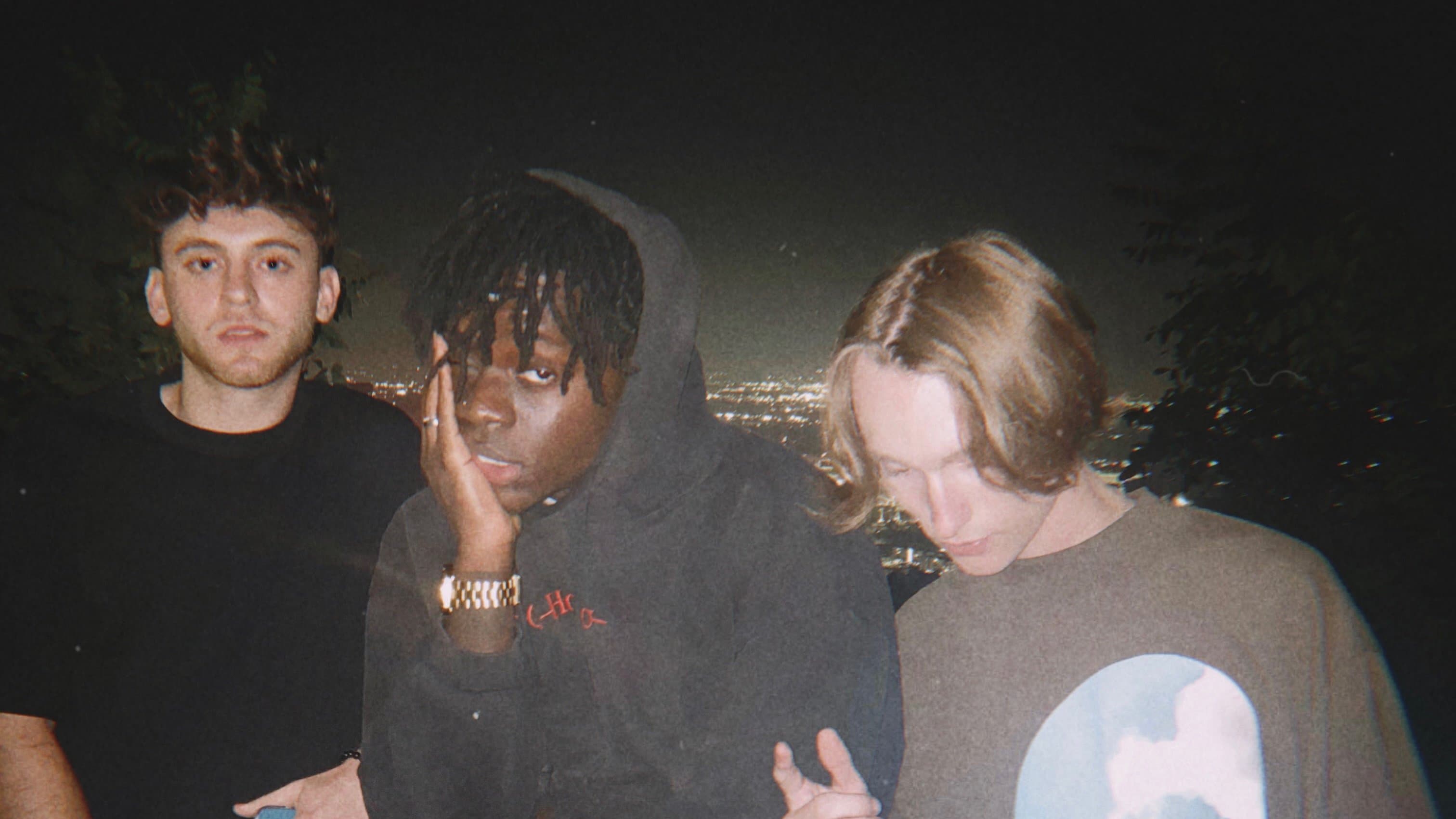 Three people on a hillside above the city at night